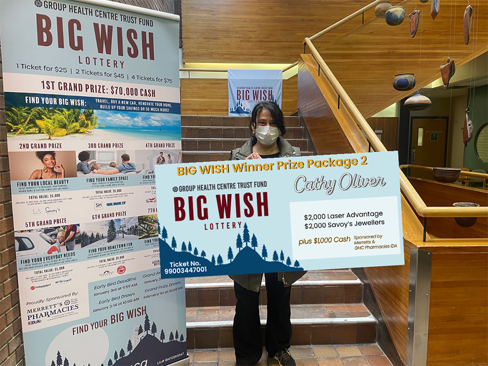 A women hold a giant presentation cheque in front of a staircase in the Group Health Centre Building