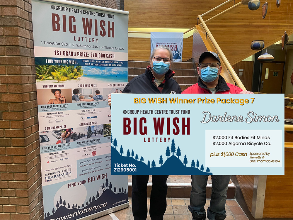 A man and a women hold a giant presentation cheque in front of a staircase in the Group Health Centre Building