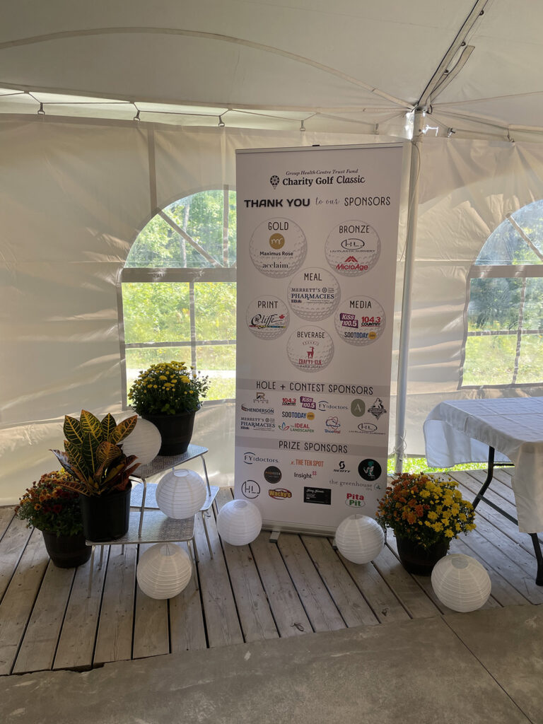 A sponsorship banner inside a large white event tent surrounded by potted plants
